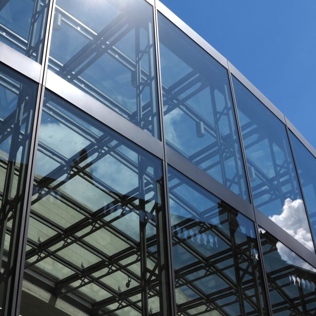 A modern glass building under a clear blue sky, with reflections visible on the surface of the building.